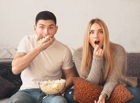 Happy couple watching interesting film at home on tv and eating popcornの写真素材