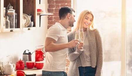 Cheers to us. Young couple drinking champagne and smiling in the kitchen at home, panoramaの写真素材