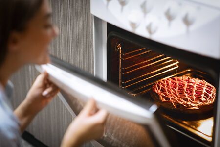 Young housewife baking fresh pie in oven, free space