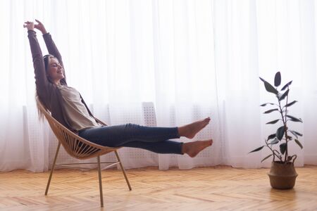 Full relax. Happy girl stretching her body, resting near window at home, empty spaceの写真素材