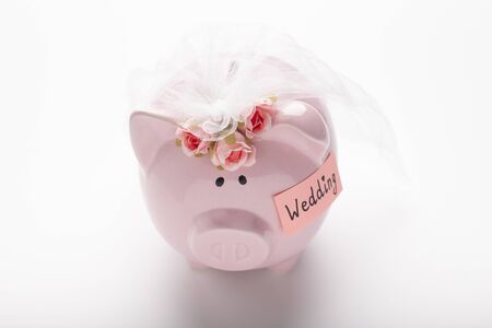 Piggy bank decorating by flowers with wedding budget money on white table background, saving money for marriage conceptの写真素材