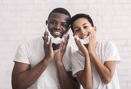 Funny Afro Father And His Preteen Son Having Fun While Shaving In Bathroom, Putting Foam To Chin As a Beardの写真素材