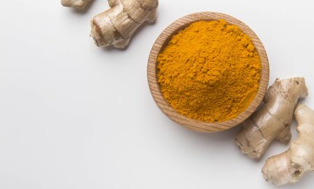 Turmeric powder in a wooden bowl and fresh turmeric curcuma root isolated on white background, copy space.の写真素材