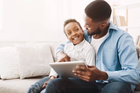 Afro father and daughter using tablet, ordering clothes and toys online, empty spaceの写真素材