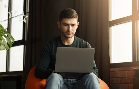 Busy Freelancer Guy Working On Laptop Sitting In Beanbag Chair At Home. Freelance Career Concept