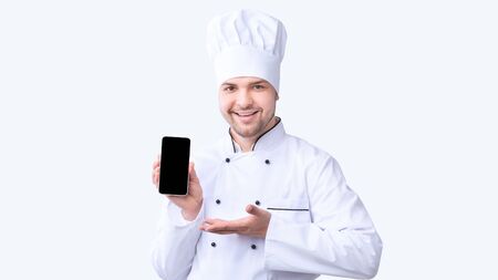Restaurant Chef Showing Cellphone With Empty Screen Recommending Food Delivery Service Standing On White Studio Background. Panoramaの写真素材
