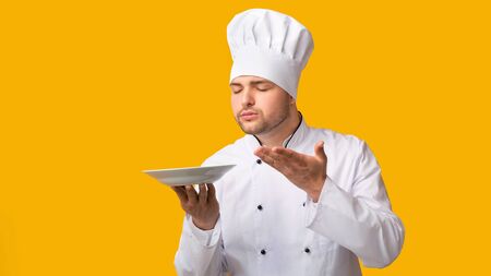 Chef Man Smelling Invisible Dish Holding Empty Plate Posing Over Yellow Background. Studio Shot, Panoramaの写真素材