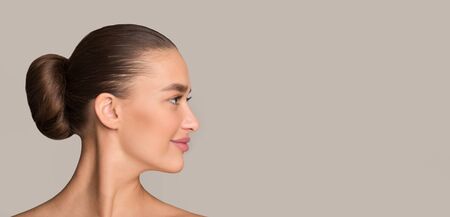 Hairstyle concept. Woman with dark hair in bun, profile portrait, grey background panorama with free spaceの写真素材