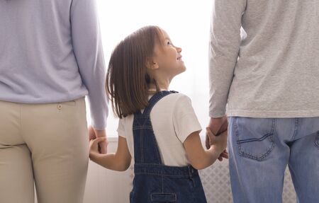 Adoption Concept. Cute Little Girl Holding Hands With Her Unrecognizable Mom And Dad, Looking Up At Father, Cropped, Rear Viewの写真素材