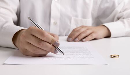 Wife signing divorce settlement and going through divorce signing papers, panorama, wedding rings