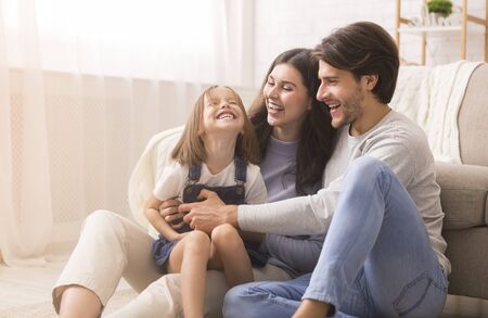 Family Love. Playful Parents Tickling Their Little Daughter, Having Fun Together At Home In Living Room, Free Spaceの写真素材