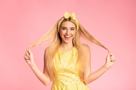 Enjoying Life. Smiling blonde girl playing and touching her long beautiful hair over pink studio wall, copyspaceの写真素材