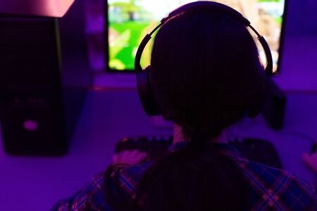 Unrecognizable Female Gamer Playing Computer Shooter Game Sitting At Desktop PC In Dark Room. Selective Focus, Rear Viewの写真素材