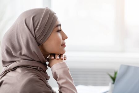 Profile portrait of relaxed saudi businesswoman in hijab sitting at wokplace with thoughtful face expression, thinking about business strategy, side viewの写真素材
