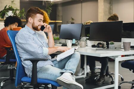 Young man discussing financial document with client on mobile phone in modern office, free space