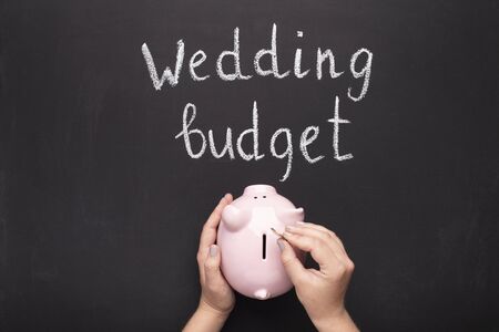 Hand collecting coins into piggy bank over chalkboard background. Family future budget concept.の写真素材