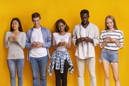 Young international friends staying in row over yellow background, using mobile phones