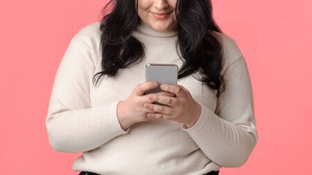 Unrecognizable overweight girl using smartphone, downloading new app, texting with friends on pinkの写真素材