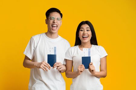 Emotional young asian man and woman holding passports with tickets