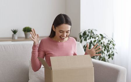Overjoyed millennial woman opening cardboard box with order, received parcel package, panorama, copy...