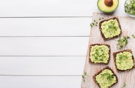 Healthy breakfast with rye bread, avocado spread and microgreen on board on white rustic wood...