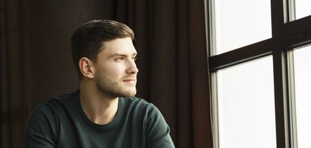 Millennial Guy Portrait. Confident Young Man Looking Aside Sitting Near Window In Modern Loft Interior Indoor. Copy Spaceの写真素材