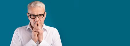 Thinking About Solution. Pensive mature man in eyewear looking at camera isolated over blue wall, panorama, copyspaceの写真素材