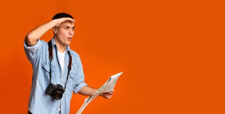 Shocked traveler with map and camera looking at empty space over orange background, panorama
