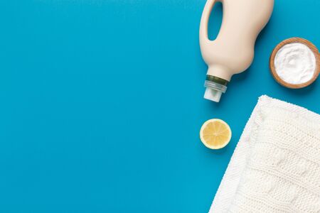 Eco friendly natural cleaners for bio washing. Baking soda, lemon, plastic bottle with conditioner and towel on blue background, copy spaceの写真素材