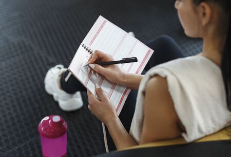 Workout planning. Young woman making her workout schedule in notebook indoors, above view
