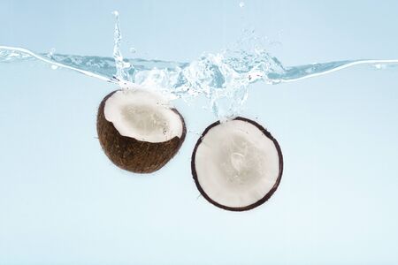 Coconut halves flying into clear water with splashes on blue backgroundの写真素材