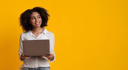 Work Opportunities Online. Pensive Afro Woman With Laptop Computer In Hands Looking Away On Yellow Background, Panorama With Free Spaceの写真素材