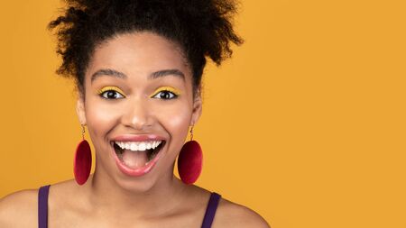 So Emotional. Overjoyed black girl with open mouth isolated over yellow studio wall, looking at...