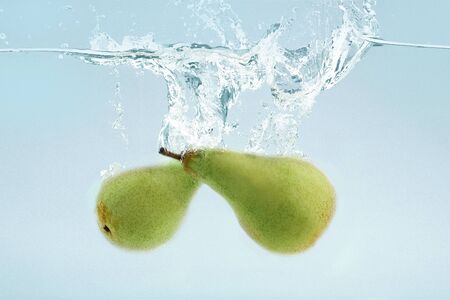 Two fresh green pears falling into transparent water on blue backgroundの写真素材