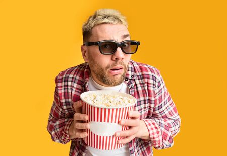 Disgust and shock from film. Surprised guy funny holding bucket of popcorn, close upの写真素材