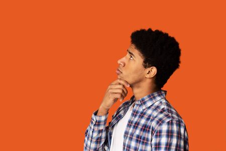 Problem solution concept. Young African-American man deep in thought on color background, side view....