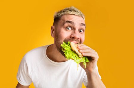 Unhealthy food concept. Funny guy eating burger, eyes wide open, close upの写真素材
