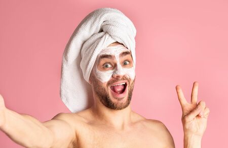 Man skin care and selfie. Millennial guy with mask on his face shows peace signの写真素材