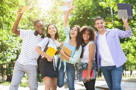 Portrait of joyful college students posing outdoors after passing exam, celebrating success and...
