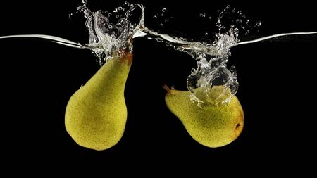 Pair of juicy pears dropping into clear water with splash on black background, panoramaの写真素材