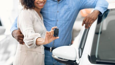 Buying Automobile. Unrecognizable Couple Showing New Car Key Hugging Standing In Dealership Shop. Panorama, Cropped, Shallow Depthの写真素材