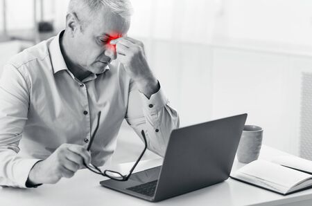 Sinus Pain. Sad mature man suffering from sinusitis, holding his nose, black and white photo with red sore zone, copyspaceの写真素材
