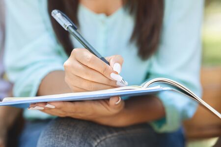 Unrecognizable female student sitting outdoors, making notes, preparing for exams at university or college, writing in workbook, closeupの写真素材