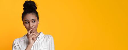 Not Sure. Doubtful black woman thinking about something, touching her lip and looking away on yellow...