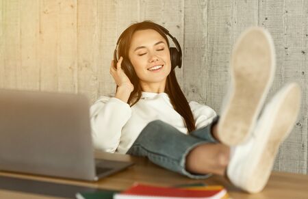 Freelance girl enjoys music in headphones with feet on the table. Sun flare, free space