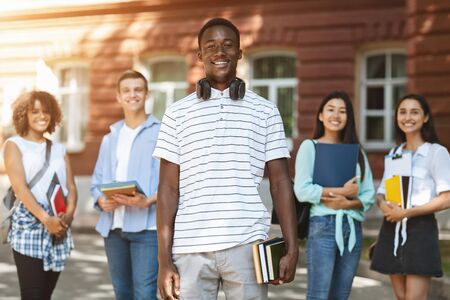 Happy African American Student Posing With His University Friends Outdoors In Campus, Selective...