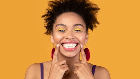 Healthy Teeth, Dental Care Concept. Afro woman widely smiling and pointing fingers at her whitened...