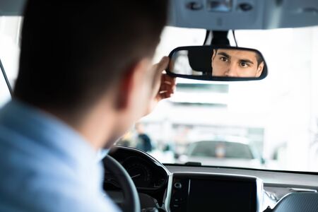 Young Man Checking Mirrors Sitting In Drivers Seat Testing Buying Auto In Dealership Store