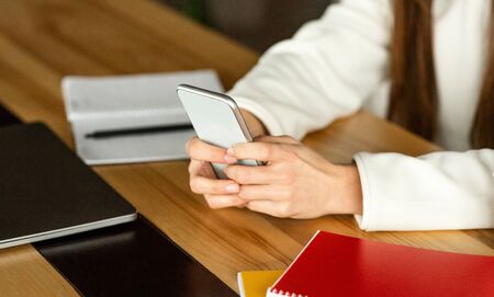 Modern technologies at work concept. Freelance girl works with smartphone, cropped