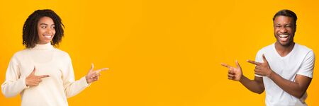 Happy African American man and woman pointing at blank space on yellow studio background, panoramaの写真素材